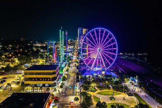 Aerial view of the Myrtle Beach SkyWheel glowing bright purple on a dark night with other city lights around it.