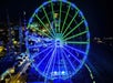Aerial view of the Myrtle Beach SkyWheel at night with half of it glowing bright blue and the other half green.