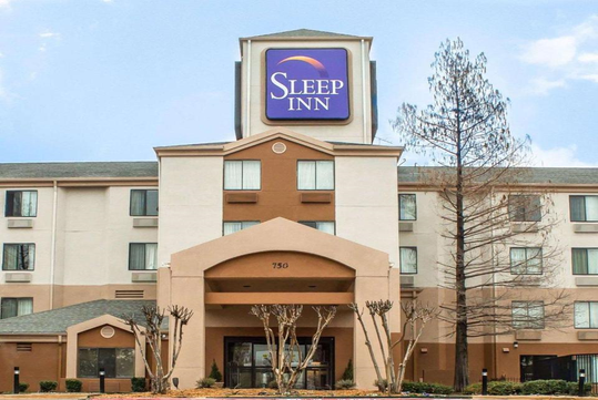 Front view of Sleep Inn hotel with a sign, featuring a tan and beige exterior and multiple windows.