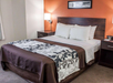 A hotel room with a neatly made double bed, two bedside tables with lamps, and an abstract framed picture above the headboard.