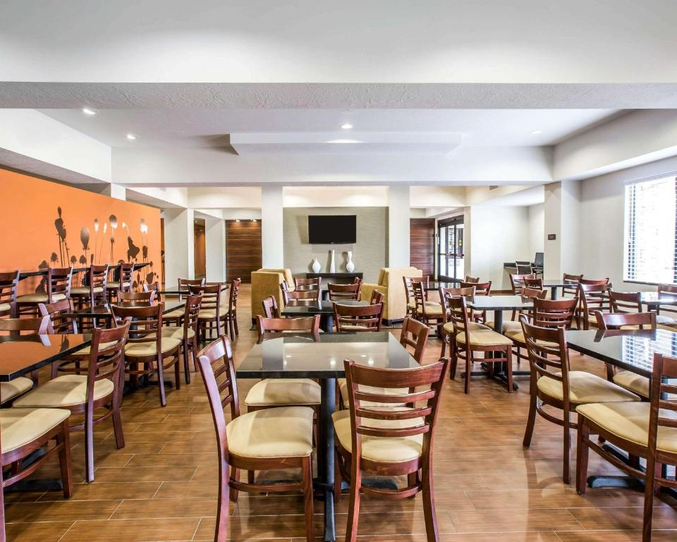 Hotel dining area with multiple wooden tables and chairs, parquet flooring, and an orange accent wall with floral designs. A TV is mounted on a wall in the background.