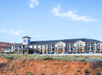 A three-story hotel with a sign, "Sleep Inn," set against a backdrop of red desert terrain and a blue sky with scattered clouds. Several cars are parked in front.
