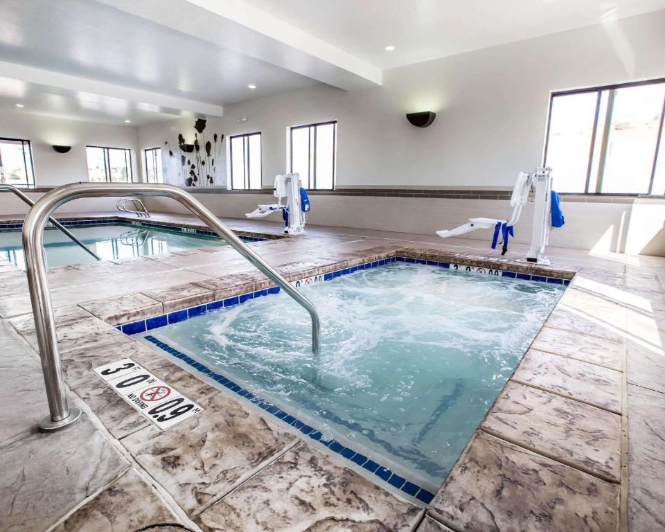 Indoor pool area with a bubbling hot tub in the foreground, stainless steel handrail, and swimming pool visible in the background. Large windows provide natural light.