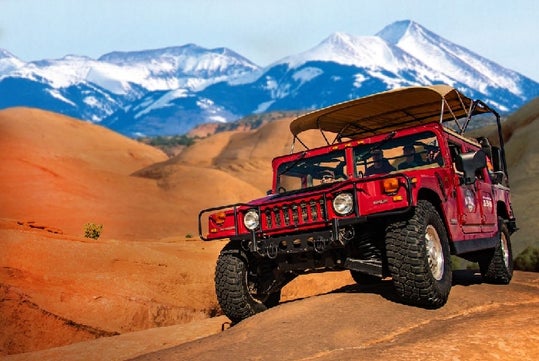 The tour Hummer making its way through the petrified sand dunes with a great view of the mountains on the Slickrock Safari Hummer Adventure Tour in Moab Utah.