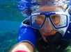 Person wearing a blue diving mask and snorkel takes a close-up selfie underwater, with the water's surface and aquatic environment visible.