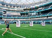 Person throwing a football at targets on a large green field inside a stadium.