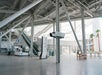 Spacious indoor area with escalators, tall metal beams, and palm trees. Signs for directions and information are visible.