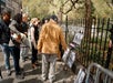 A group of people stand on a sidewalk looking at black-and-white artwork displayed on the fence of a park.