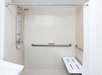 Accessible shower with white tiles, a handheld showerhead, grab bars, and a white folding bench.