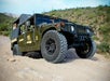 A green off-road vehicle with large tires navigates a rocky terrain in a desert landscape.