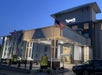 Exterior view of a Spark hotel at dusk, with illuminated signage, an American flag, and parked cars visible.