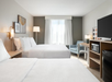 The room features two queen beds, a TV, mini-fridge, microwave, and a desk for comfort and convenience.