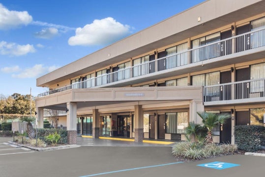 Two-story hotel building with balconies, wheelchair accessible parking, and palm trees in the foreground.