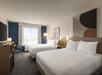 2 Queen beds, working area, and a flat-screen TV inside a guest room.