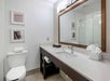 A modern bathroom with a large mirror, sink, and toilet. Towels are neatly placed on the counter and toilet. Wall decorations include two framed pictures.