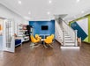 Modern waiting room with yellow chairs, a blue accent wall, snacks on shelves, and a staircase on the right.