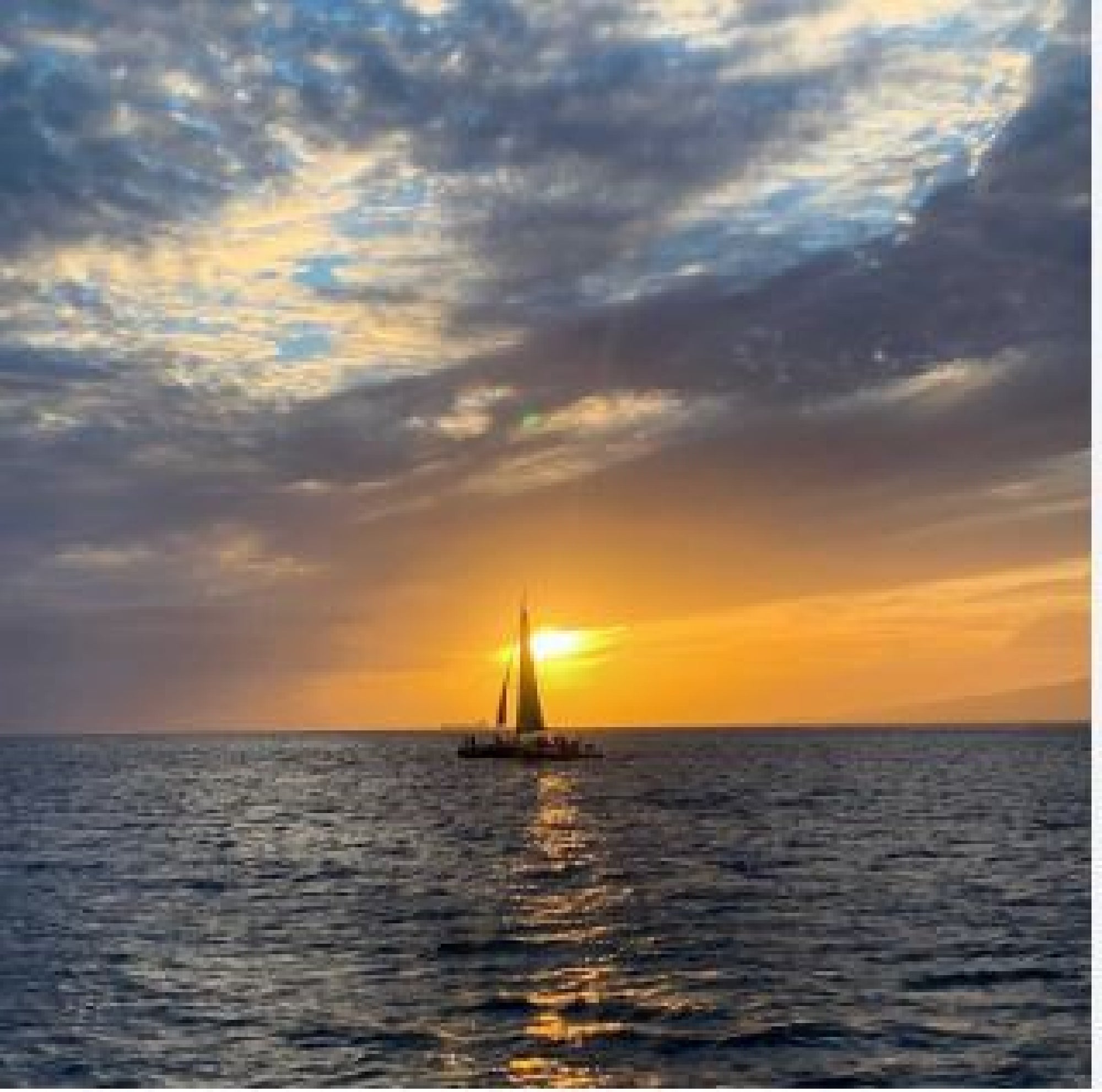 A sailboat glides on the ocean during sunset, with dramatic clouds and golden sunlight reflecting on the water.
