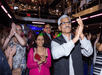 People dancing and clapping on the dance floor at the Spirit of New York Signature Dinner Cruise with dining tables on the upper level visible behind them.