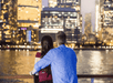 A couple facing away from the camera leaning against the railing of the Spirit of New York Signature Dinner Cruise boat looking at the city.