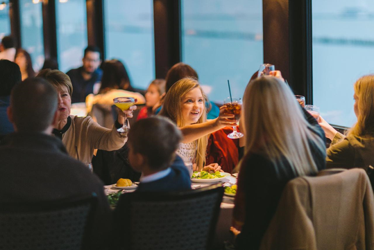 A group of people seated at a dining table in a restaurant, raising their glasses for a toast.