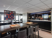 Lounge with bar, chessboard on a high table, and large connect four game. Black chairs surround table. Ceiling lights illuminate the space.