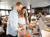 People at a buffet, selecting food from various dishes in a dining area.