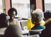 A group of people sitting at a restaurant table, engaging in conversation. The focus is on a woman smiling, with a glass of water in front of her.