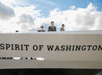 People standing on the deck of a boat with "SPIRIT OF WASHINGTON" written on it, under a partly cloudy sky.