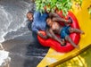 A father and son tightly grip the handles as they ride in a red inflatable tube, plunging down from Dragon's Den at Splish Splash.
