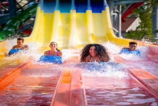 Four guests splashing into water at the bottom of a yellow and orange waterslide at Splish Splash Water Park.