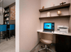 A small business center with a computer and printer on a white desk, a beige office chair, and shelves full of knick knacks above the desk.
