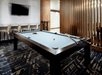 A pool table with balls and cues laying on it and a bar and chairs on the back wall with a TV above them at the SpringHill Suites by Marriott.