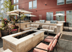 A large light colored stone outdoor seating area with several umbrellas, a fire pit, and two grills on a sunny day in Columbus, Ohio.
