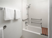 Accessible bathroom with white towels, a bathtub featuring grab bars, a handheld showerhead, and a wooden shower bench.