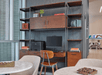A built in desk with with a computer, printer, and office chair in the middle and shelves with books and other knick-knacks in a hotel lobby.