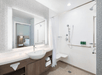 Modern bathroom with a sink and mirror on the left, a walk-in shower with a curtain and mounted bench on the right, and toiletries on a shelf. Doorway shows part of a bedroom.