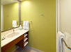 Bathroom with a sink, mirror, and towel holder on a light green wall. Shelves below the sink hold towels and toiletries. A glass shower door is partially visible on the right.