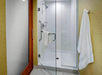 Glass-enclosed shower with a towel rack holding a white towel and washcloth. Beige walls and a wooden door are visible.