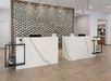 Modern hotel reception with two white marble desks, geometric metal wall art, and wood-patterned floor.