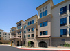 A multi-story hotel building with beige exterior, multiple windows, and a red tile roof under a clear blue sky.