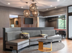 Modern lounge area with a gray sectional sofa, round coffee table, and geometric pendant lights. A TV is mounted on a slatted wooden partition.
