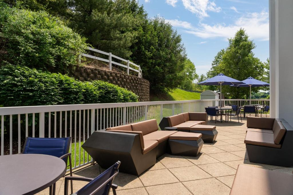 Outdoor patio with modern seating, tables, and umbrellas, surrounded by greenery and a white fence on a clear day.