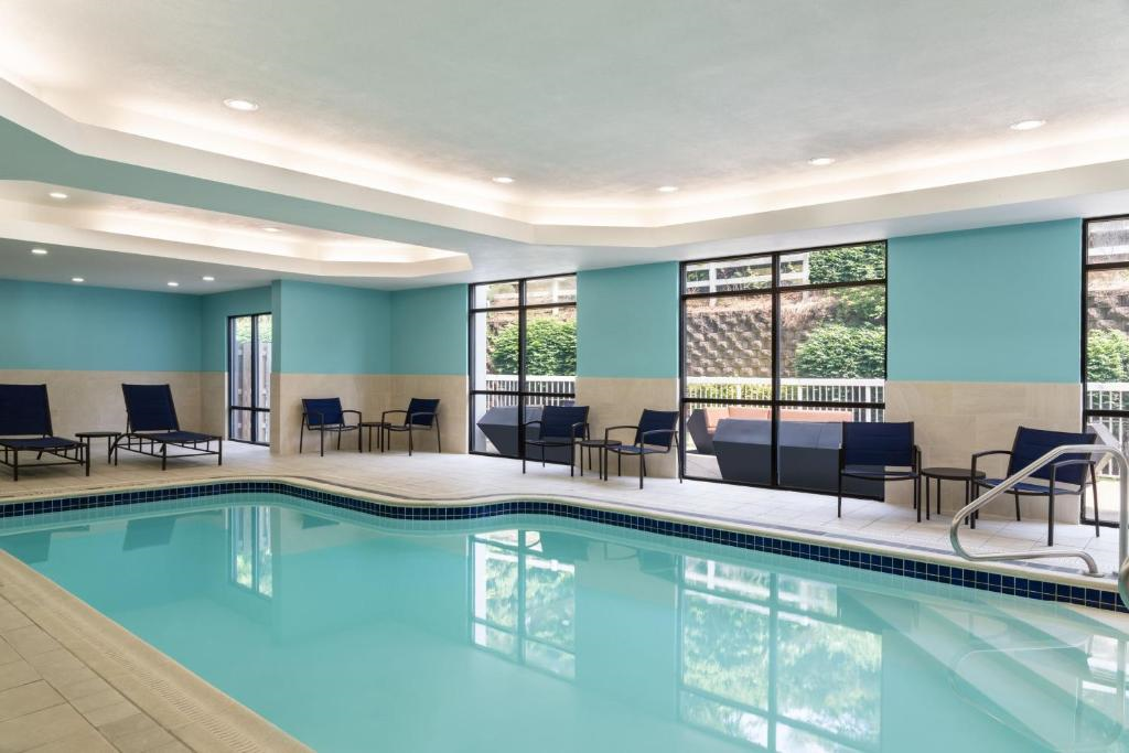 Indoor swimming pool with blue water, surrounded by lounge chairs and large windows. The walls are light blue with beige accents.