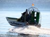 An airboat with a caged propeller moves quickly across the water, creating a trail of spray behind it.