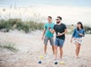 Three people playing bocce ball on a sandy beach; one man throws the ball while others watch.