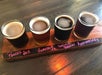 A wooden flight board holds four glasses of beer labeled Ponce’s Ale, Anastasia IPA, French Brown, and Anniversary.