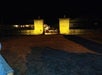 Nighttime view of an illuminated stone entrance with two pillars leading to a dimly lit street.