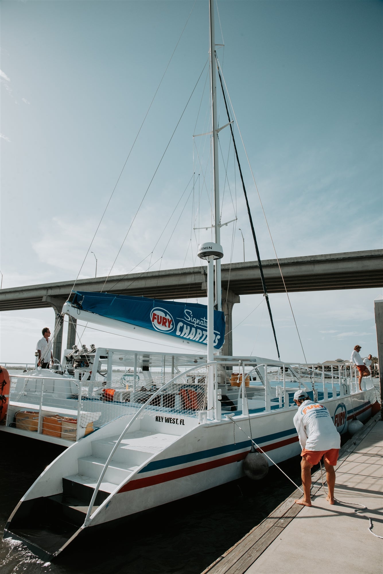 A catamaran docked at a marina under a clear sky, with a man securing a rope in the foreground.