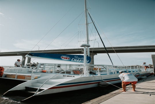 A catamaran docked at a marina under a clear sky, with a man securing a rope in the foreground.