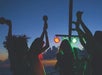 Silhouettes of people dancing and holding maracas at sunset, with colorful stage lights in the background.